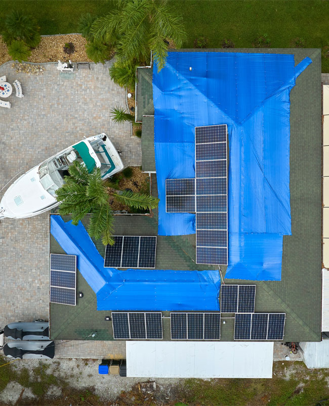 Blue tarp over parts of a roof with solar panels. 