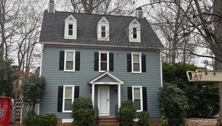 Large white home with new Hardie siding and black shutters surrounded by trees.
