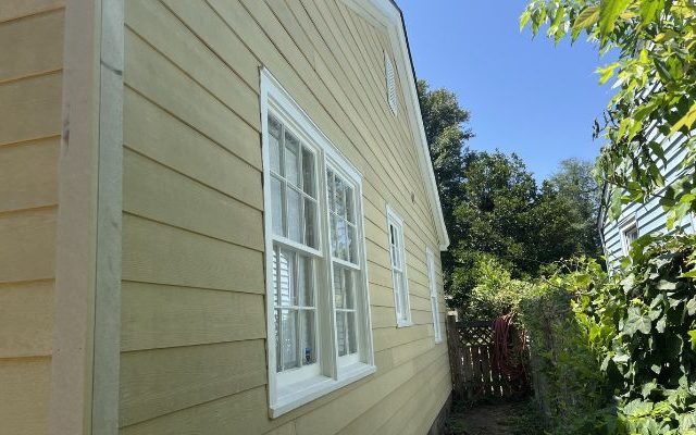 Side view of home after vinyl siding installation with new yellow siding and white trim.