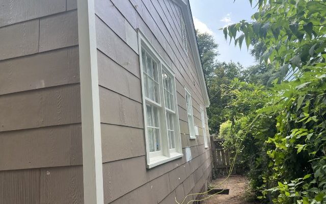 Side view of home before vinyl siding repair with worn brown siding and white trim.