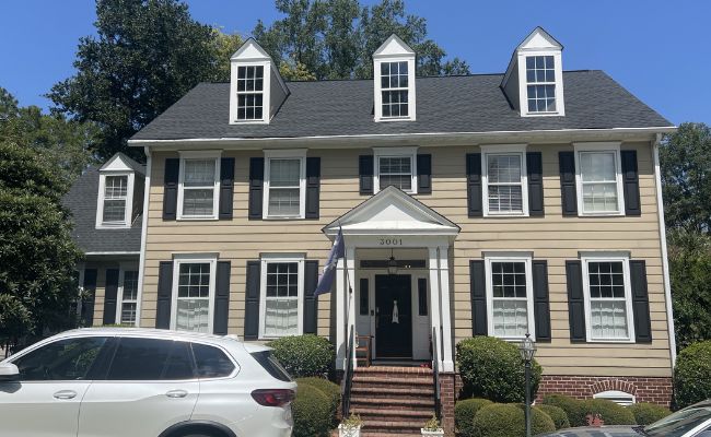 Large two-story home with tan siding, black shutters, and a new roof installation.