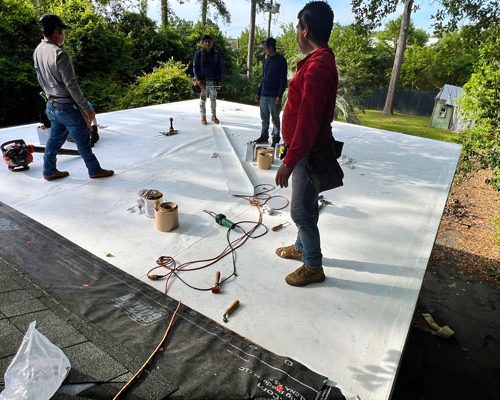 flat-roof-membrane-underlayment-midlands-sc Workers installing a flat roofing membrane over roof decking.
