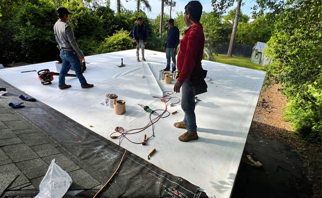 Workers installing a flat roofing membrane over roof decking.