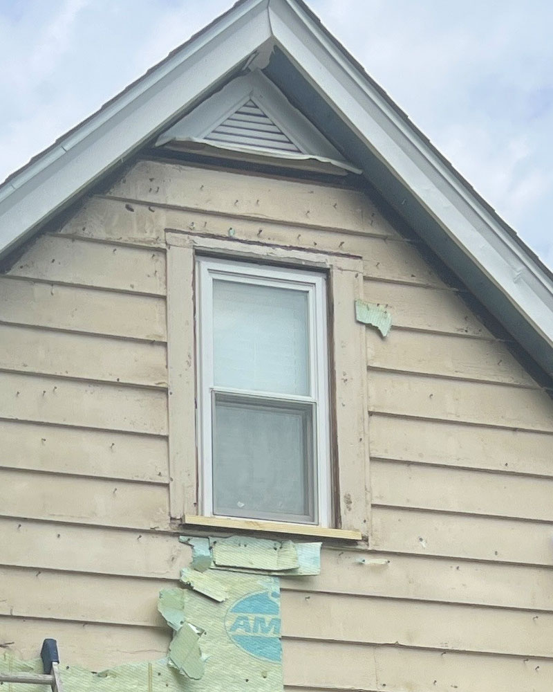 Weathered siding being removed from a gable wall around an upper window.