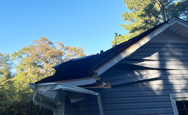 Damaged roof with collapsed gable and torn shingles before roof repair.