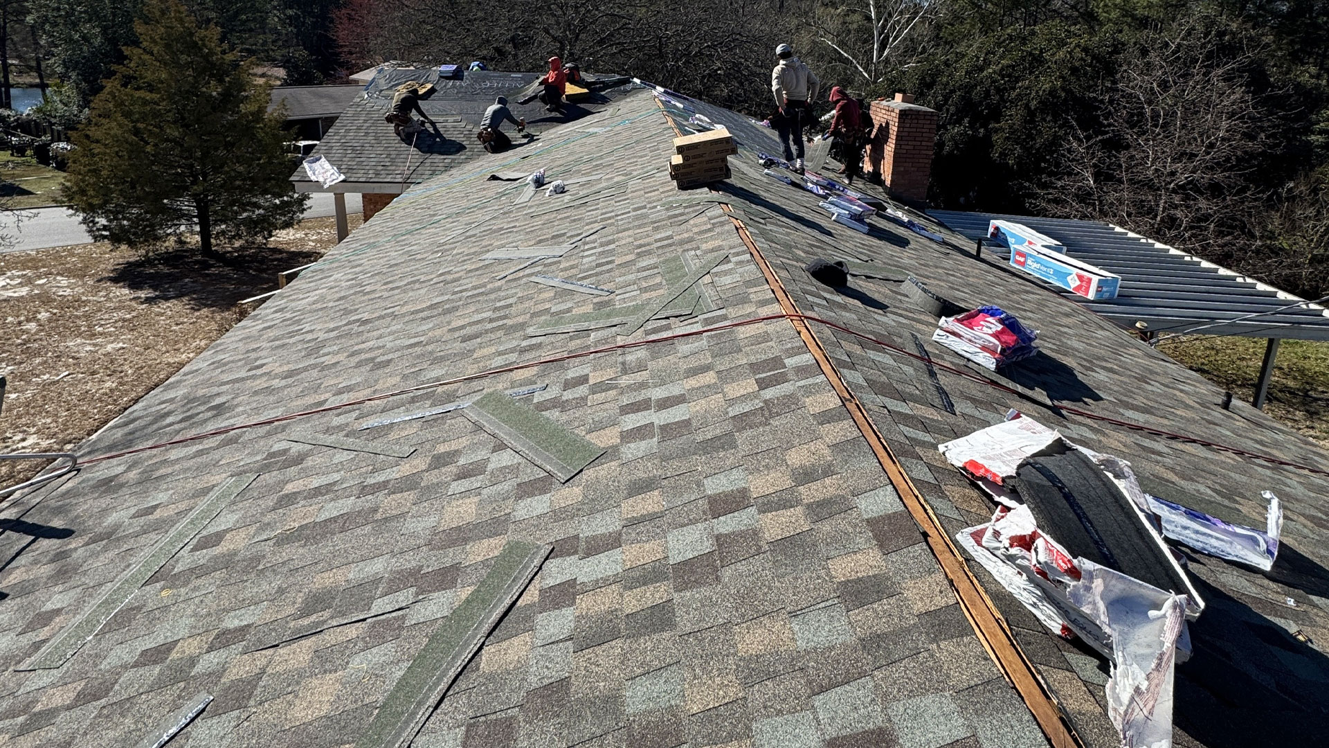 Roofers installing underlayment and shingles on a two-story home.