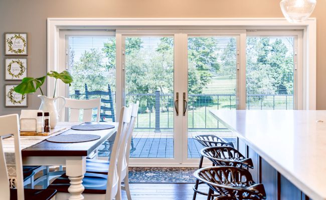 Interior kitchen view looking out through white ProVia sliding glass patio doors toward an outdoor wooden deck and backyard.